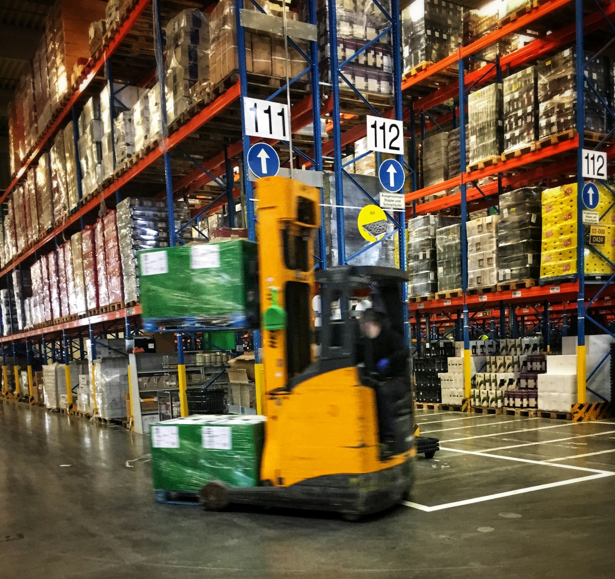 Heftruck rijdt met pallets door een magazijn met hoge palletrekken