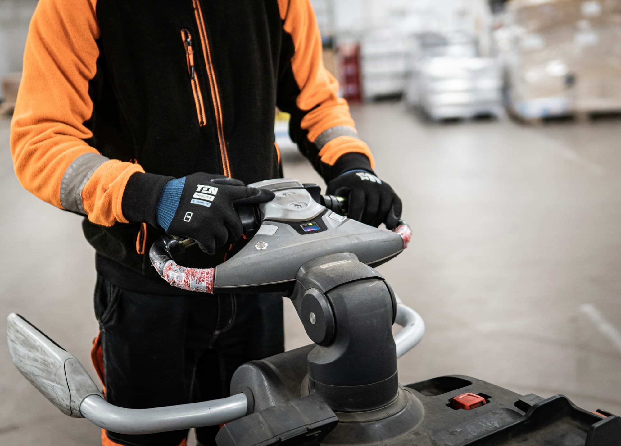 Magazijnmedewerker met werkhandschoenen aan de hendel van een elektrische palletwagen